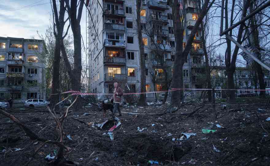 A woman with a dog walks among the rubble of a house damaged after a Russian strike on residential area in Kyiv, Ukraine, on Thursday, April 16, 2026.