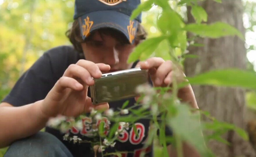 A young boy takes pictures in the field as featured in "Is School Enough?"