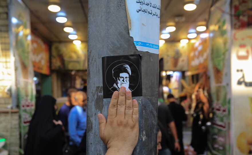 A pilgrim touches a sticker bearing a portrait of slain Iranian Supreme Leader Ali Khamenei affixed to a utility pole on a street in Karbala during the Arbaeen pilgrimage, as millions of pilgrims gather at the Imam Hussein Shrine to commemorate the annual religious occasion.