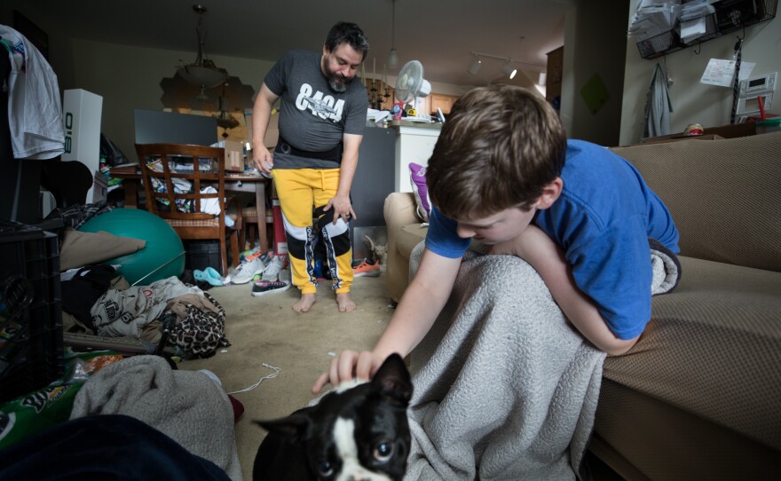 Michael Marquette adjusts his brace after his recent hip surgery, while stepson Anthony Calabro, 12, plays with Spring.