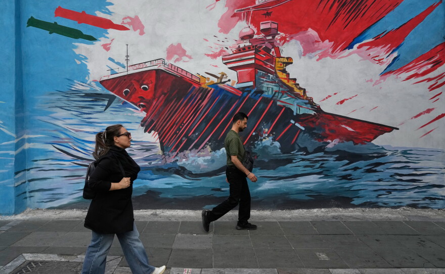 People walk past a mural depicting a U.S. aircraft carrier under missile attack by Iran in downtown Tehran, on May 17. The two countries agreed to a ceasefire but strikes have continued including U.S. military strikes against Iranian targets on Monday.