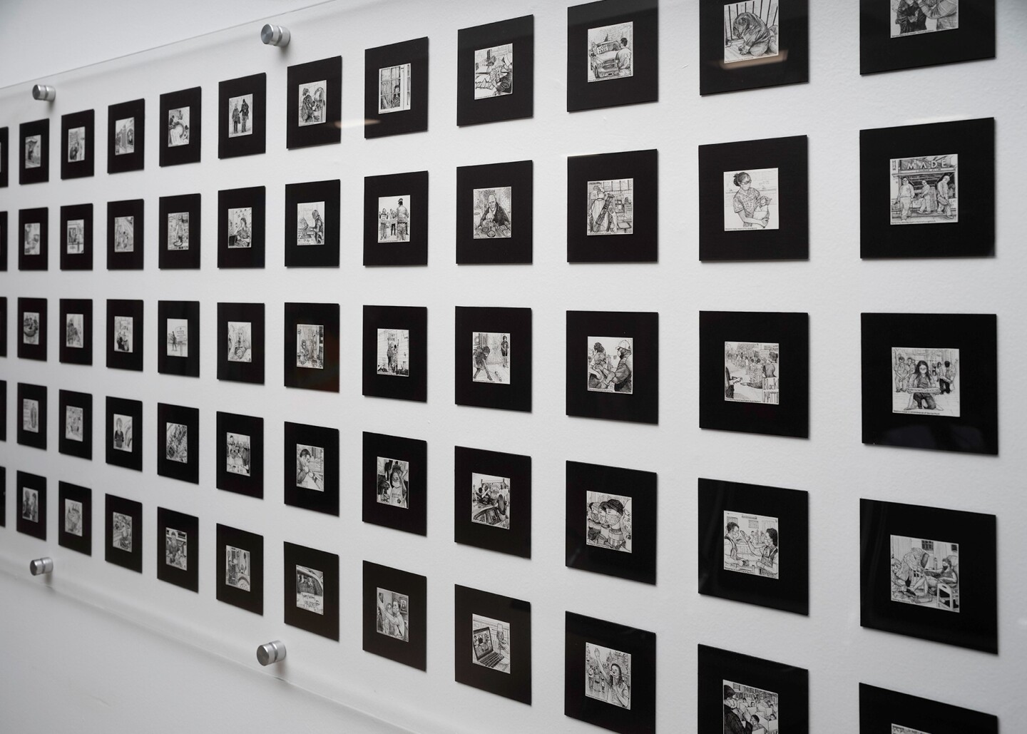 A close-up of a hundred small drawings framed in thick black matting, organized uniformly on the wall.