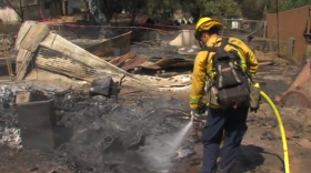 A firefighter sprays down smoldering hot spots on a burned down structure in San Marcos on May 16, 2014.