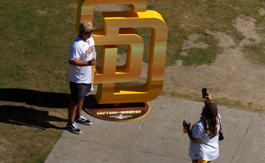 A fan poses for a photo in front of a San Diego Padres Logo display before game two of the NLCS at Petco Park on Oct. 19, 2022. 