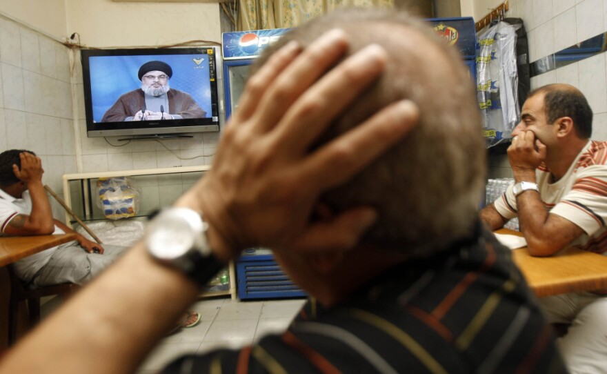 Lebanese men watch Hezbollah's leader Hassan Nasrallah give an address July 2. Nasrallah says authorities will never be able to arrest four members of his militant group who have been indicted in the murder of former Lebanese Prime Minister Rafik Hariri.
