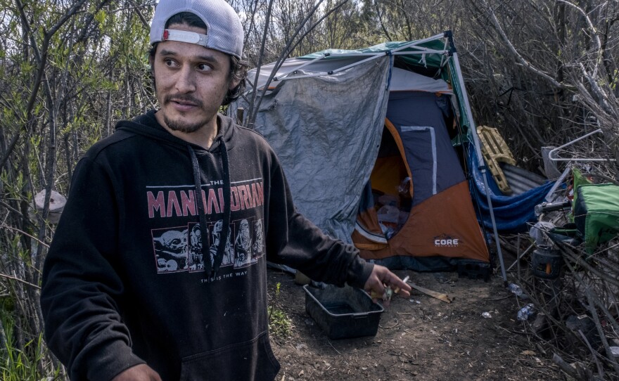 Gabriel smokes a cigarette in front of his tent along the outskirts of "the jungle" in Chula Vista, March 8, 2023.