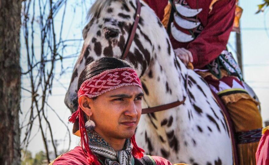 Sawgrass, of Creek descent, shows off traditional adornments and attire, including silver earrings, a long shirt, and a crescent-shaped silver metal gorget at the FSU Homecoming parade. Behind him, the student playing Osceola wears a patchwork symbol for Fire. His horse Renegade isn't authentic to the real-life Osceola, impressive as he may be. He's an Appaloosa. Seminoles rode less showy horses.