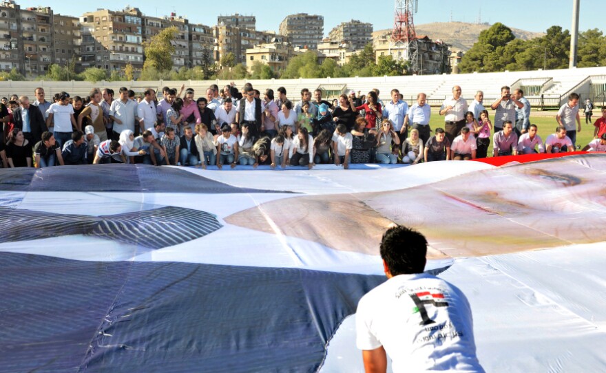 Regime supporters prepare to mount a huge poster of Syrian President Bashar al-Assad at Al-Jalaa Stadium in Damascus.