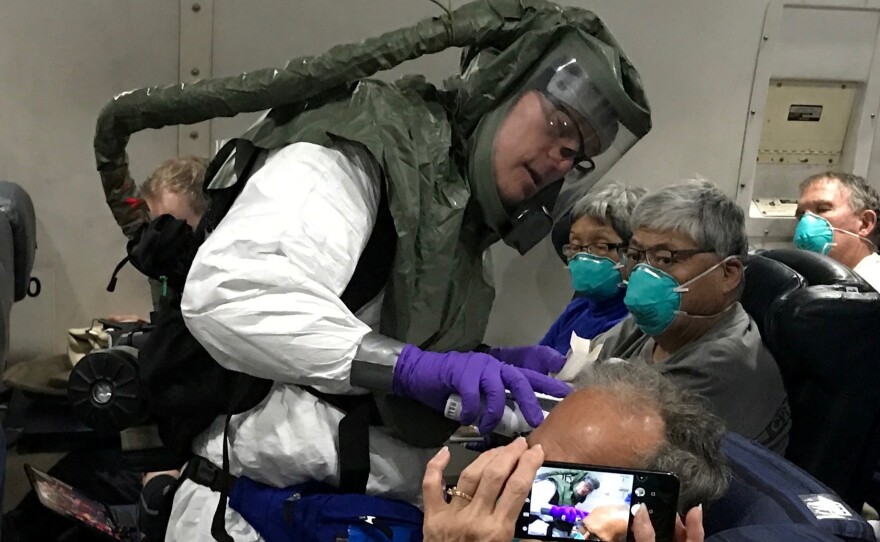 Checking for signs of COVID-19, a medical worker in a protective suit checks the temperatures of people who were on board the Diamond Princess cruise ship as they fly on a chartered evacuation plane from Japan to Lackland Air Force Base in Texas.
