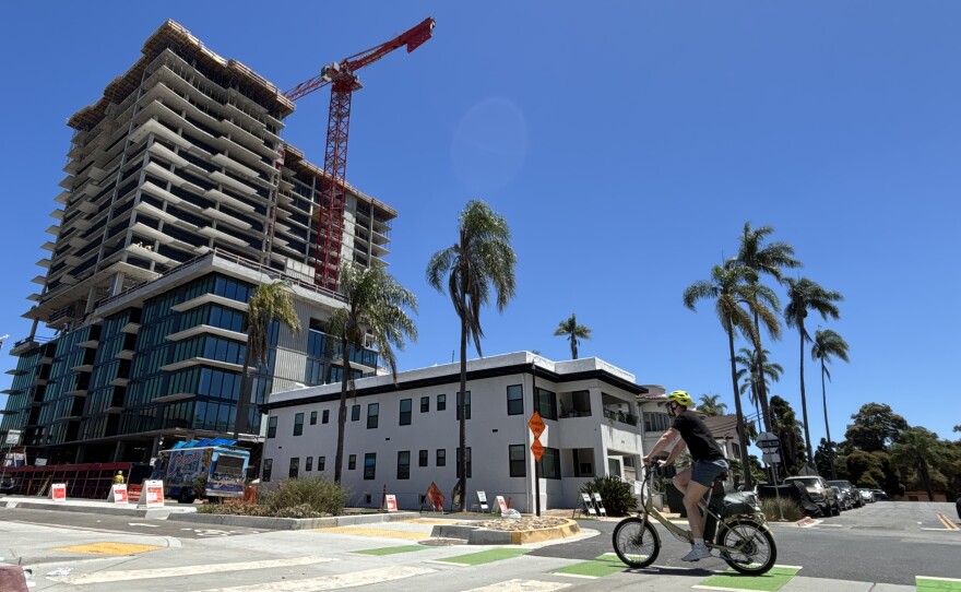 A cyclist rides by the construction site of a high-rise apartment building in Banker's Hill, July 25, 2025.