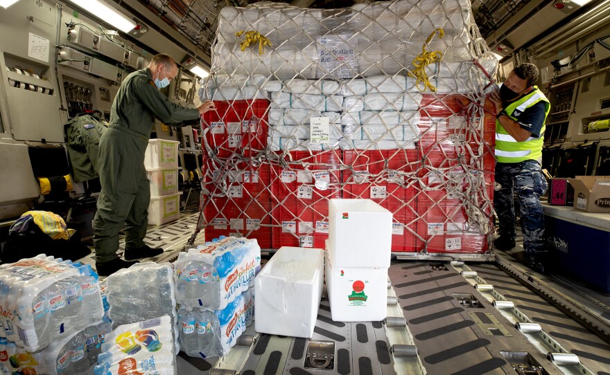 Air Force Load Master Corporal Dale Hall (left) helps secure humanitarian aid supplies for Tonga aboard an Australian aircraft.
