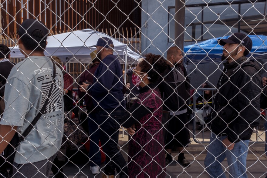 In the foreground a new chain link fence near the Tijuana side of the San Ysidro Port of Entry, behind that regular border crossers, and in the background are Ukrainian war refugees waiting for their chance to claim asylum in the United States, April 4, 2022.