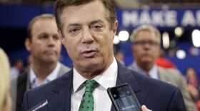 Trump Campaign Chairman Paul Manafort talks to reporters on the floor of the Republican National Convention at Quicken Loans Arena in Cleveland as Rick Gates listens at back left, July 17, 2016. 