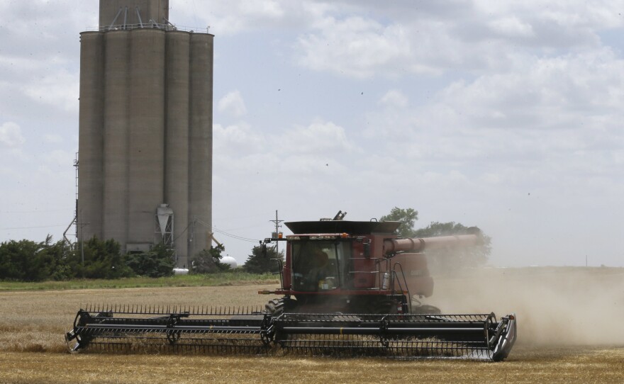A combine harvests wheat by a grain elevator near Mayfield, Kan.
