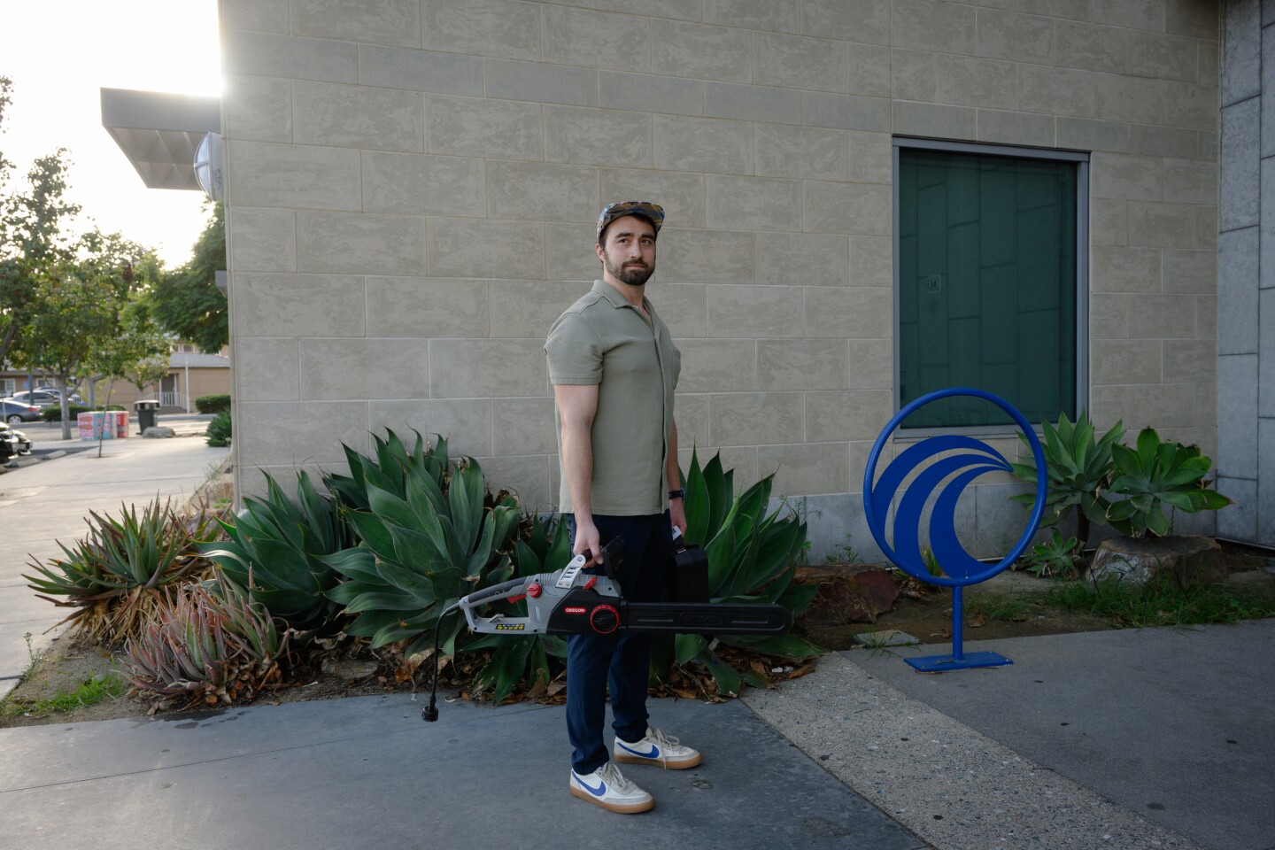 National City resident Matt Sikorski stands for a portrait outside the National City Public Library in National City, California holding an electric chainsaw and an endoscope camera that he checked out from u-Tool-ize, the library's tool lending program, in October 2025.