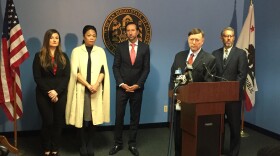 San Diego City Attorney Jan Goldsmith stands at a podium, while Benelia Santos-Hunter, second from the left, stands in the background, at a press conference announcing a settlement in Santos-Hunter's case against former San Diego Mayor Bob Filner, Feb. 2, 2016. 
