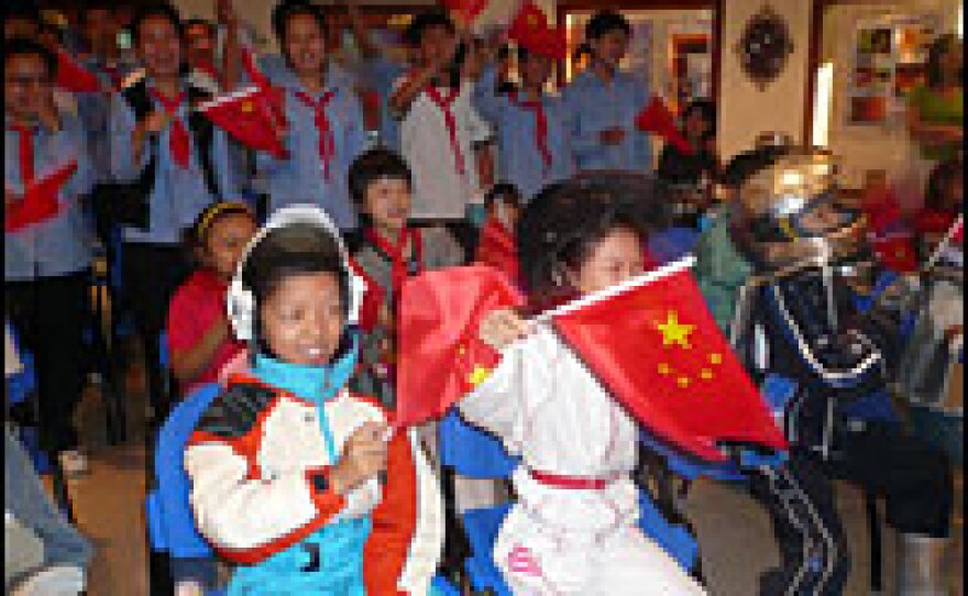 Members of the space enthusiasts club wave Chinese flags as China's first spaceman floats out of the airlock.