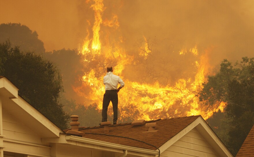Standing on a rooftop, a man looks at the Springs fire's approaching flames in California Friday. The wildfire, reportedly, 20 percent contained, might be weakened by high humidity and cooler temperatures Saturday.