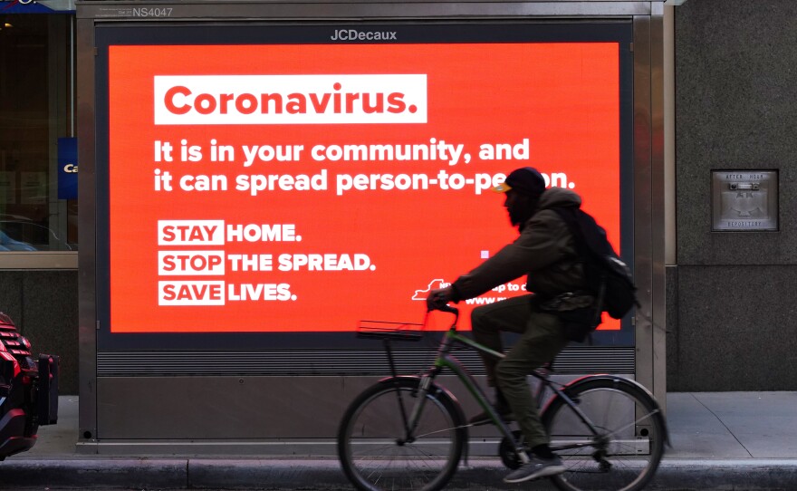 A person on a bike rides by a sign in New York City urging people to stay home in May. As the pandemic drags on, some workers are facing tough choices — balancing potential risks of unwittingly spreading the disease against the possibility of losing pay during a quarantine.