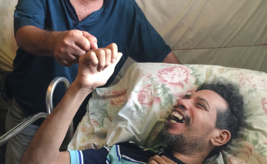 Osvaldo Martinez (left) takes care of his increasingly disabled son, Osvaldo Daniel Martinez, who is on Medicaid. With few neurologists on the island, they have not been able to get the younger Martinez an appointment with a specialist who could formally diagnose and treat him.