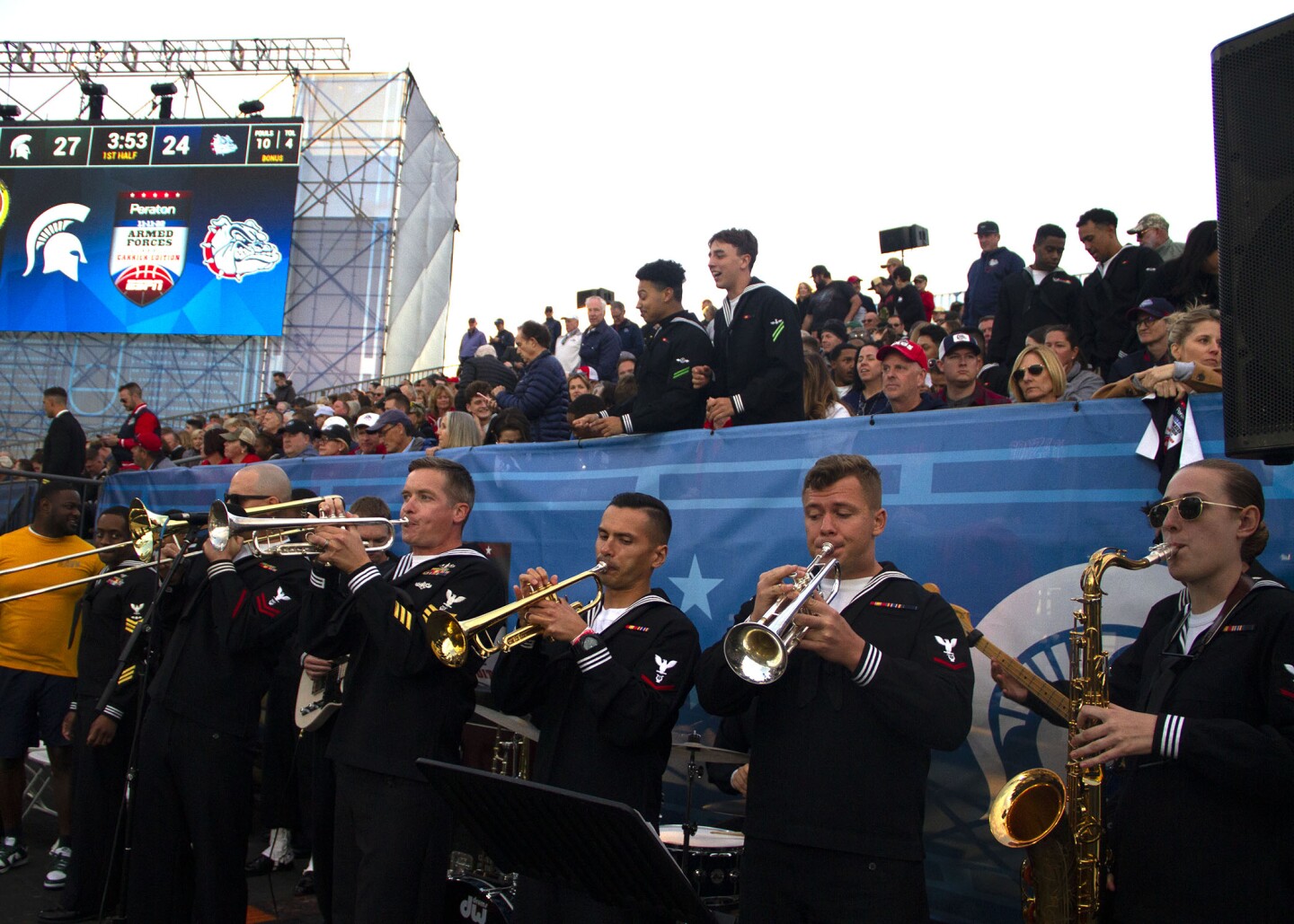 A Navy band plays while excited fans stand in the background during the Armed Forces Classic aboard the USS Abraham Lincoln on Nov. 11, 2022.