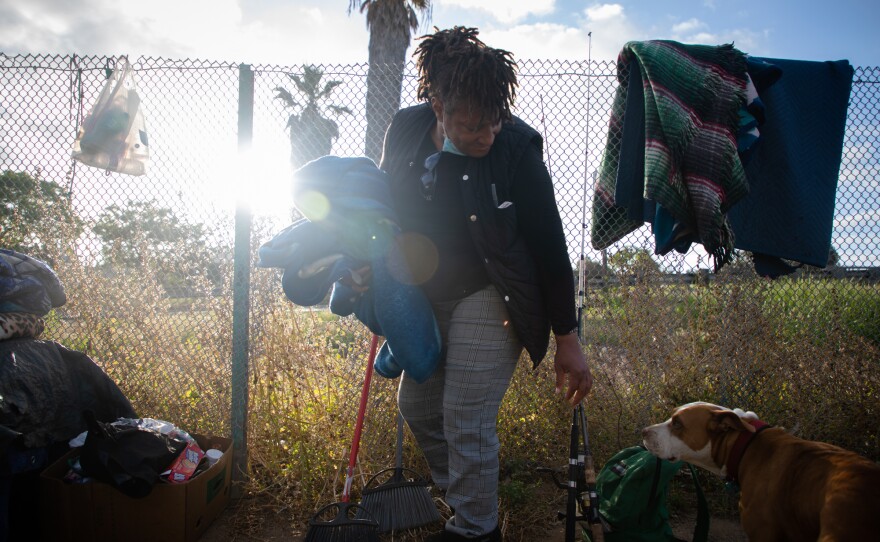 Wanita Long packs up blankets after sleeping on an area of dirt near the Interstate 5 ramp at 17th Street in San Diego, May 20, 2020.