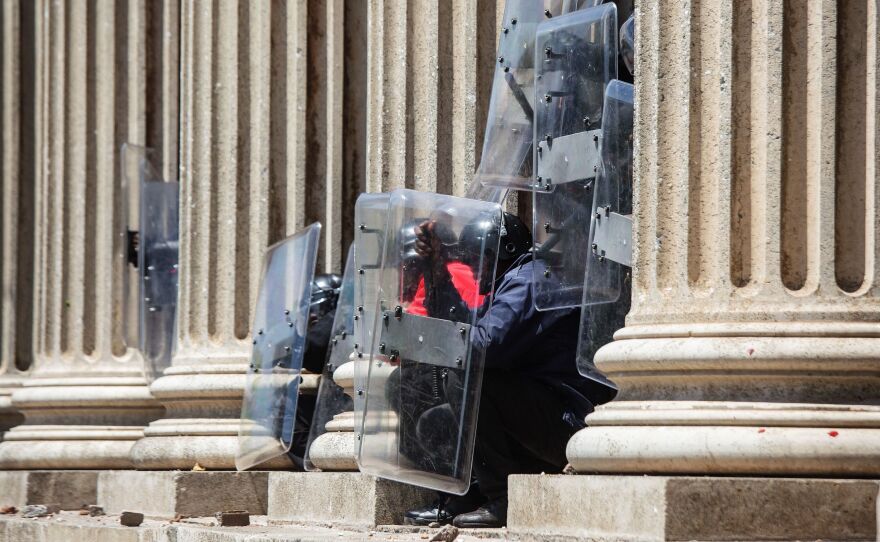 Private security guards protect themselves from stones thrown by students from the University of the Witswatersrand in Johannesburg on Monday. South African student protesters and police clashed in renewed violence as attempts to re-open the university descended into running battles on campus.