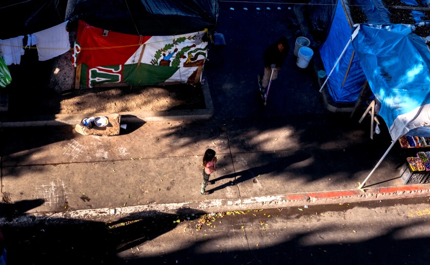A small child stands in a pool of sunlight at the migrant camp at the El Chaparral border crossing in Tijuana, November 17, 2021.<br/>