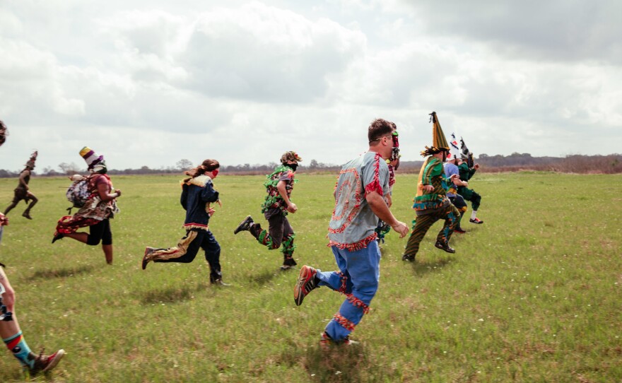 The Mardi Gras run through an open field chasing down another chicken.