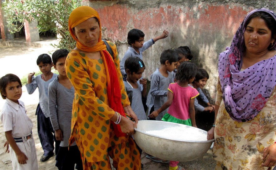 Saroj (left) helps her colleague carry a cauldron of rice to the school kitchen after washing it.