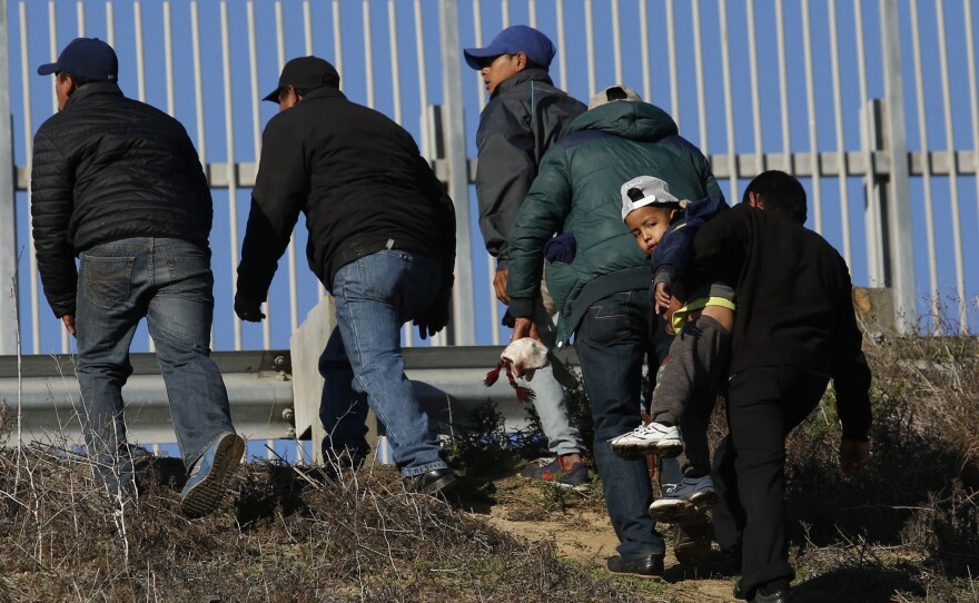 Migrants, one carrying a child, who plan to turn themselves over to U.S. border agents, walk up the embankment after climbing over a U.S. border wall from Playas de Tijuana, Mexico, last week. On Tuesday, members of the Hispanic Caucus called for improved medical facilities and trained personnel at ports of entry.