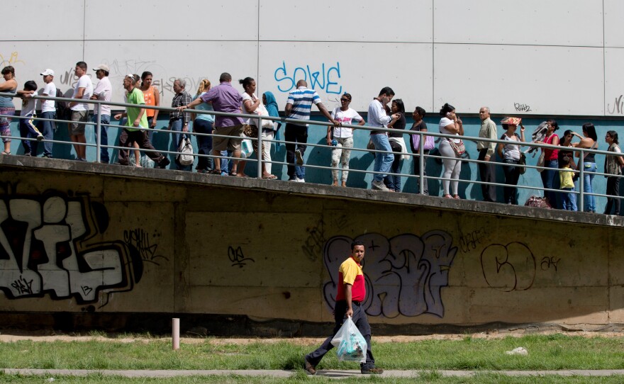 A man carries newly bought disposable diapers past a line of people waiting to enter a private supermarket to buy the same item in Caracas, Venezuela, on Jan. 16. The country's economy is in crisis, with high inflation, sinking oil revenues and shortages of many goods.