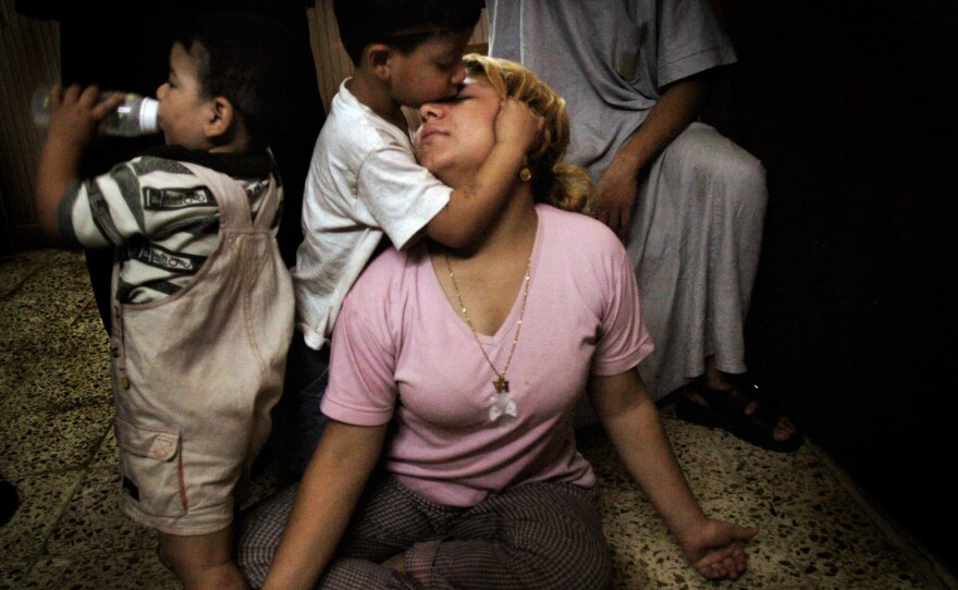 In Baghdad, Halla Hameed receives a kiss from her son Iaad Hameed, 4, while her two year-old drinks from a bottle. Halla's husband Walid Hameed, the father of her two children, was shot and killed in the violence surrounding Baghdad during the initial days of the U.S. invasion. She became a prostitute to provide for her children. A customer sits behind her. September 2, 2003