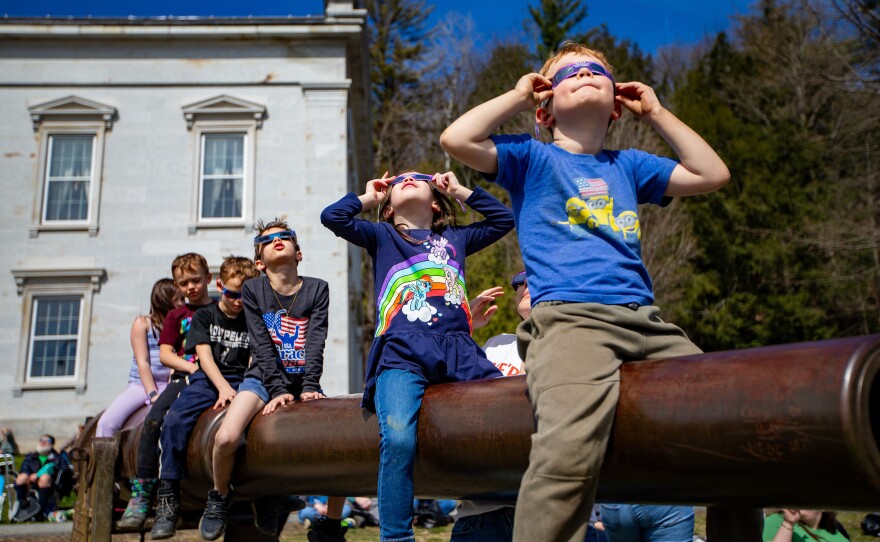 Kids watch the total eclipse begin sitting on a cannon out in front of the Vermont State Montpelier, Vermont on April 8, 2024.