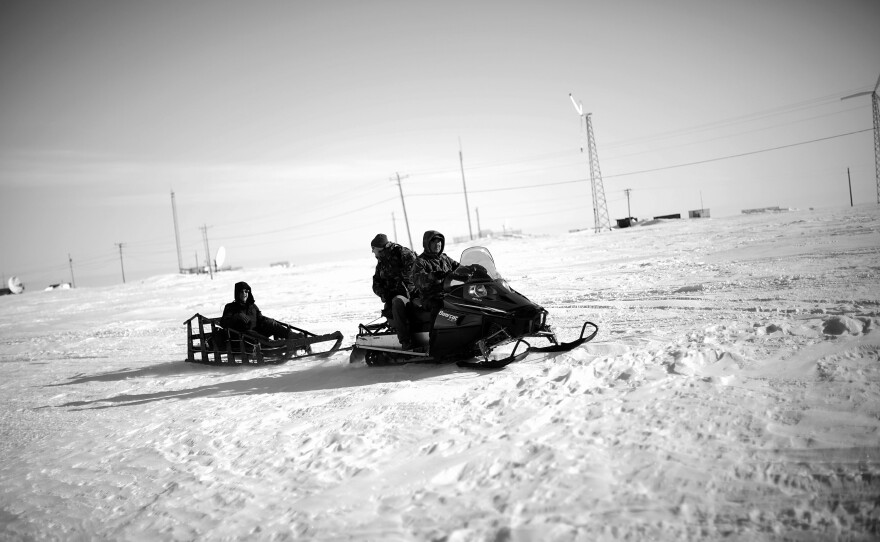 Local veterans representative Sean Komonaseak drives a snowmobile with Tommy Sowers (back seat) and Sean Foertsch across the ice to the village of Wales, Alaska.