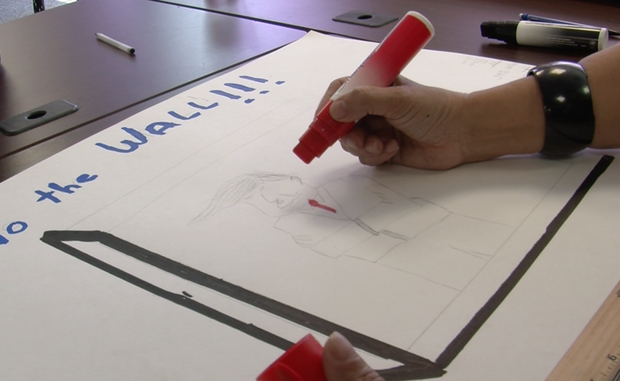 Martina Pappas sketches Donald Trump in a straitjacket, with a border fence around his body at the San Diego County Democratic Party office, May 26, 2016. 