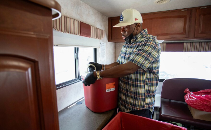 Pierson disposes a container full of used needles into a cardboard box lined with a biohazard bag to get destroyed.