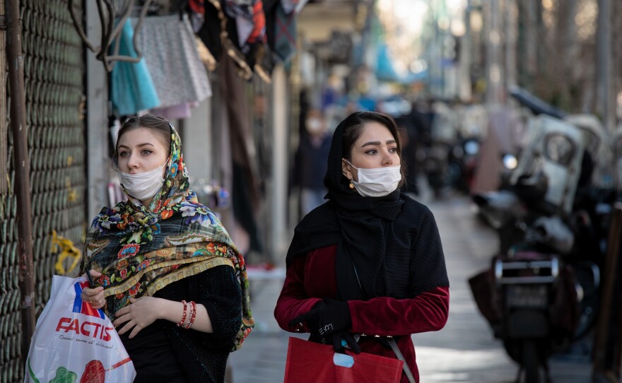 Wearing masks that cover their mouths, but not their noses, two young women walk through Tehran's Valiasr street after shopping. Under normal circumstances, the Valiasr promenade, famous for its medium budget boutiques, would be packed.