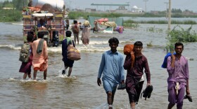People wade through a flooded area in Pakistan, that has been dealing with what people are calling "monster monsoons".