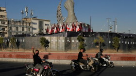 A man reacts to the camera while driving past a monument depicting the clenched fist of the late Iranian Supreme Leader Ayatollah Ali Khamenei, who was killed in U.S. and Israeli strikes on Feb. 28, and a missile at the Islamic Revolution square in downtown Tehran, Iran, Tuesday.