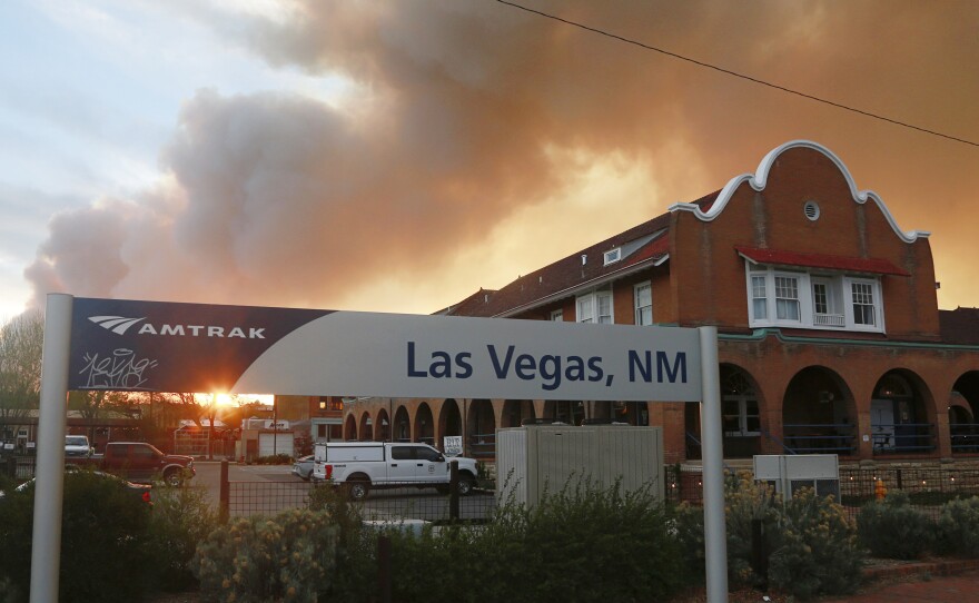 A sunset seen through a wall of wildfire smoke from the Amtrak train station in Las Vegas, N.M., on Saturday. The Castañeda Hotel, right, hosted meals for residents and firefighters this week with sponsorships from restaurants and other businesses.