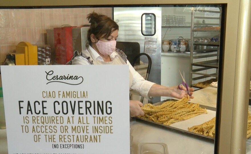 A worker making pasta at Cesarina in Point Loma with a sign requiring face covering on the premises, July 21, 2020.