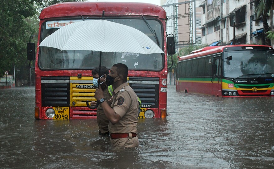 A policeman helps a public transport driver to cross a flooded street due to heavy rain caused by cyclone Tauktae in Mumbai.