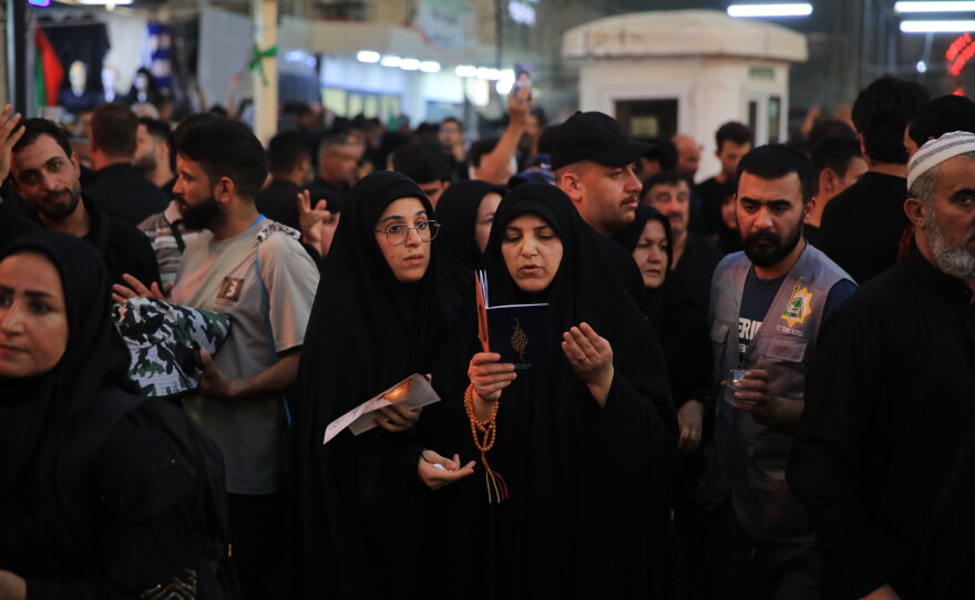 Two pilgrims recite prayers amid crowds in Karbala during the Arbaeen commemoration.