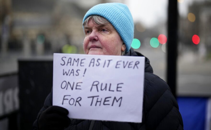 An anti-Brexit protester holds up an anti-government placard by Parliament Square, in London, Tuesday, Jan. 25, 2022.