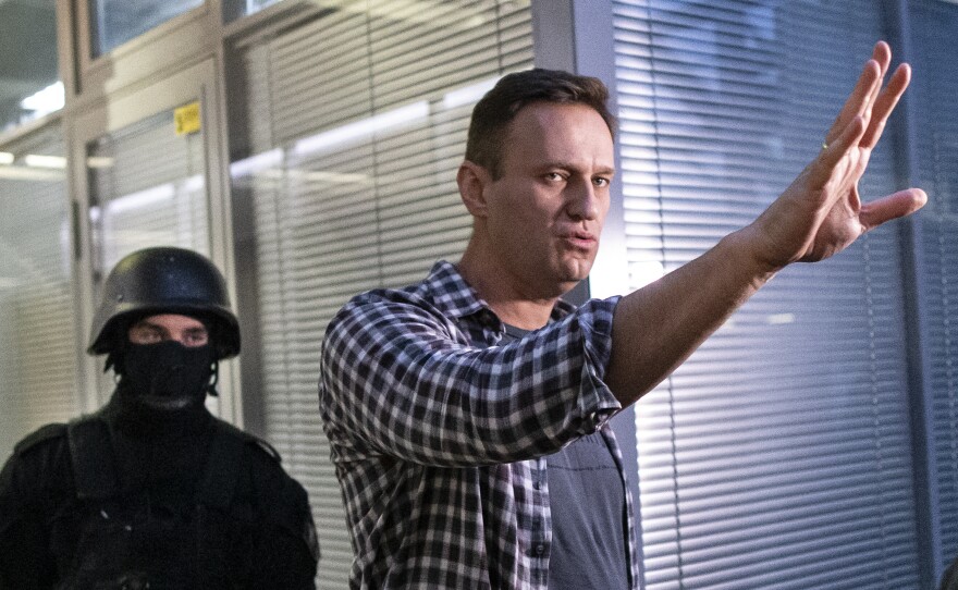 Russian opposition leader Alexei Navalny gestures while speaking to the media as a security officer guards an entrance of the Anti-Corruption Foundation office in Moscow, Russia, Thursday. The federal court bailiffs' service that conducted the Thursday raid later said he had not been detained.