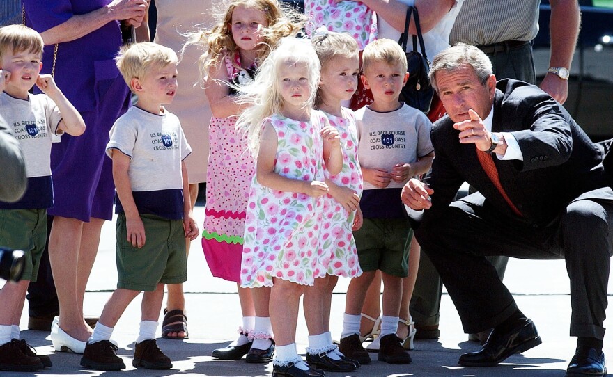 President Bush points out reporters and photographers to some of the McCaughey septuplets as they greet him at the Des Moines International Airport in Iowa in 2002.
