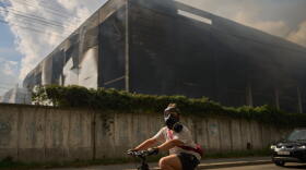 A local resident wears a gas mask as he rides a bicycle past a partially destroyed warehouse after a Russian drone attack in Brovary on the outskirts of Kyiv, Ukraine, Friday, Sept. 4, 2026.