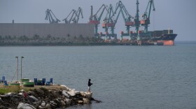 A man fishes next to shipping equipment  in Indonesia's Morowali Industrial Park in December 2025.