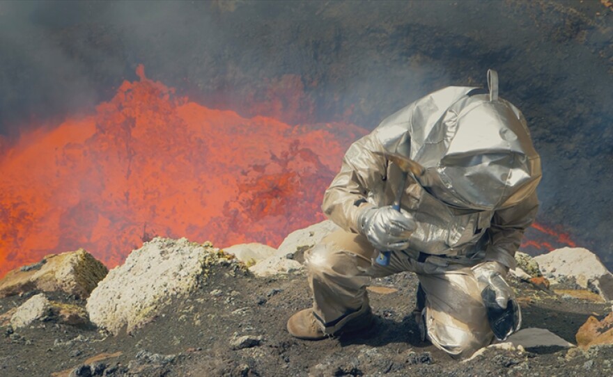 Scientist Dr. Jeffrey Marlow takes samples with the bubbling lava lake of Marum, Vanuatu behind him.